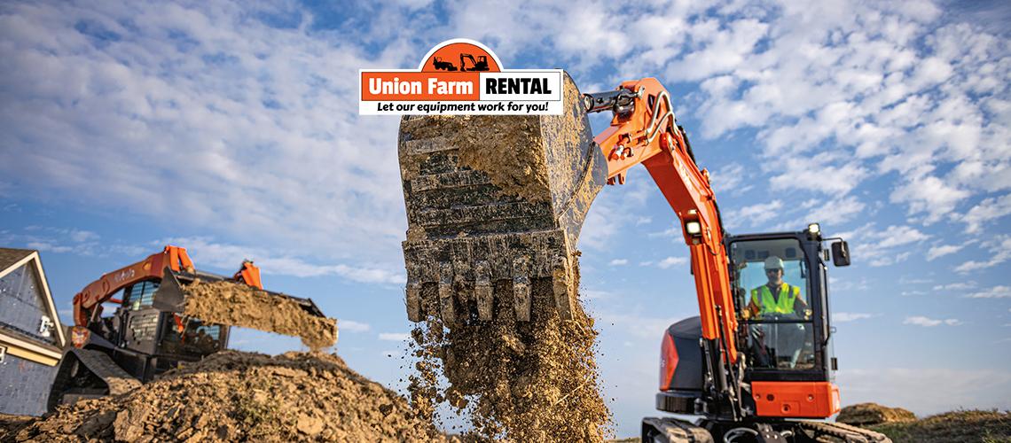 Picture of a Kubota track loader next to an excavator dropping a bucketful of dirt